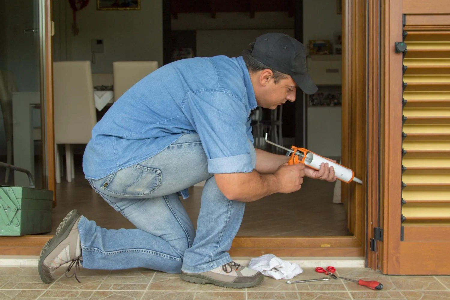 Technician kneeling to run a bead of sealant along a door frame