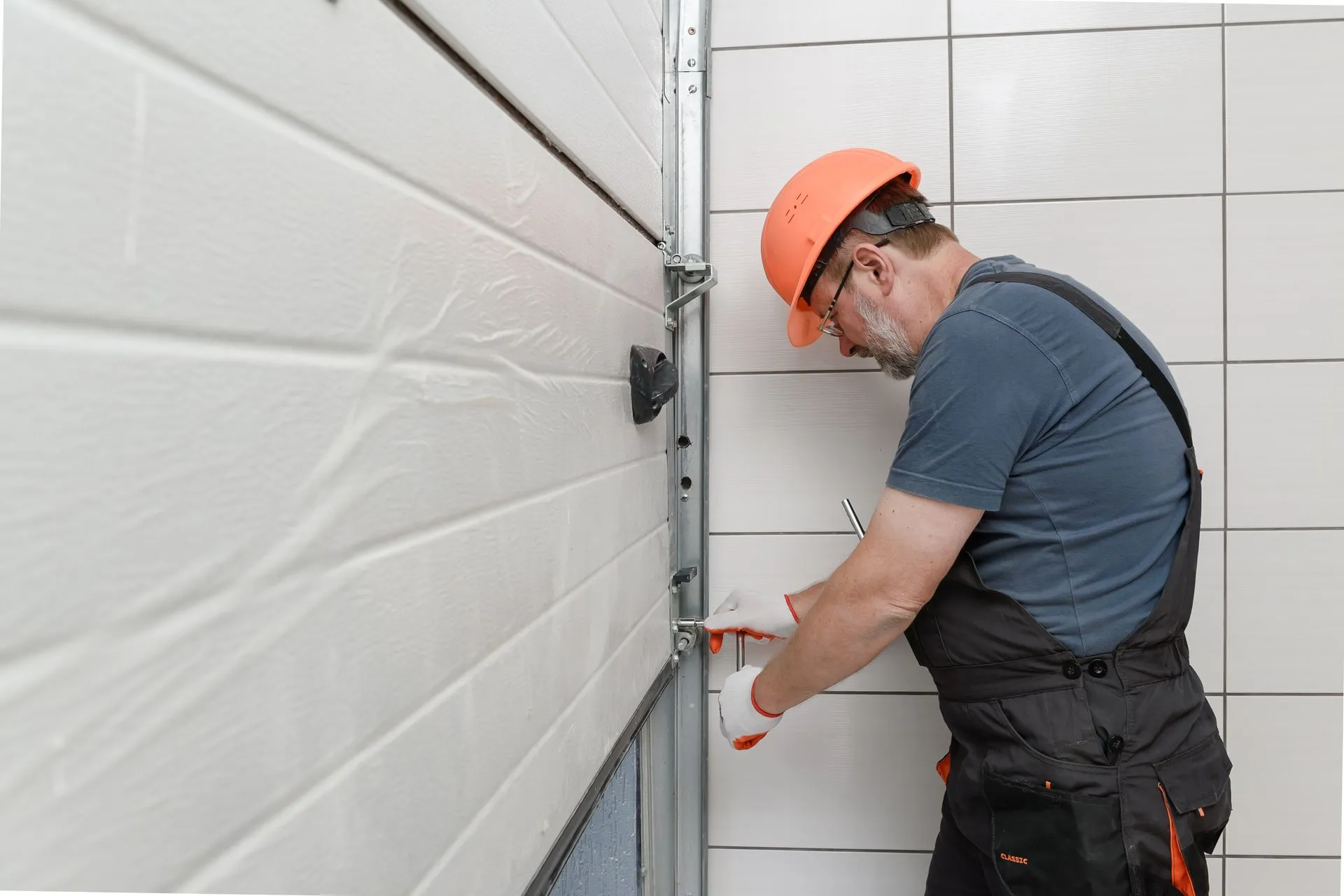Technician tightening the track hardware on a white sectional garage door