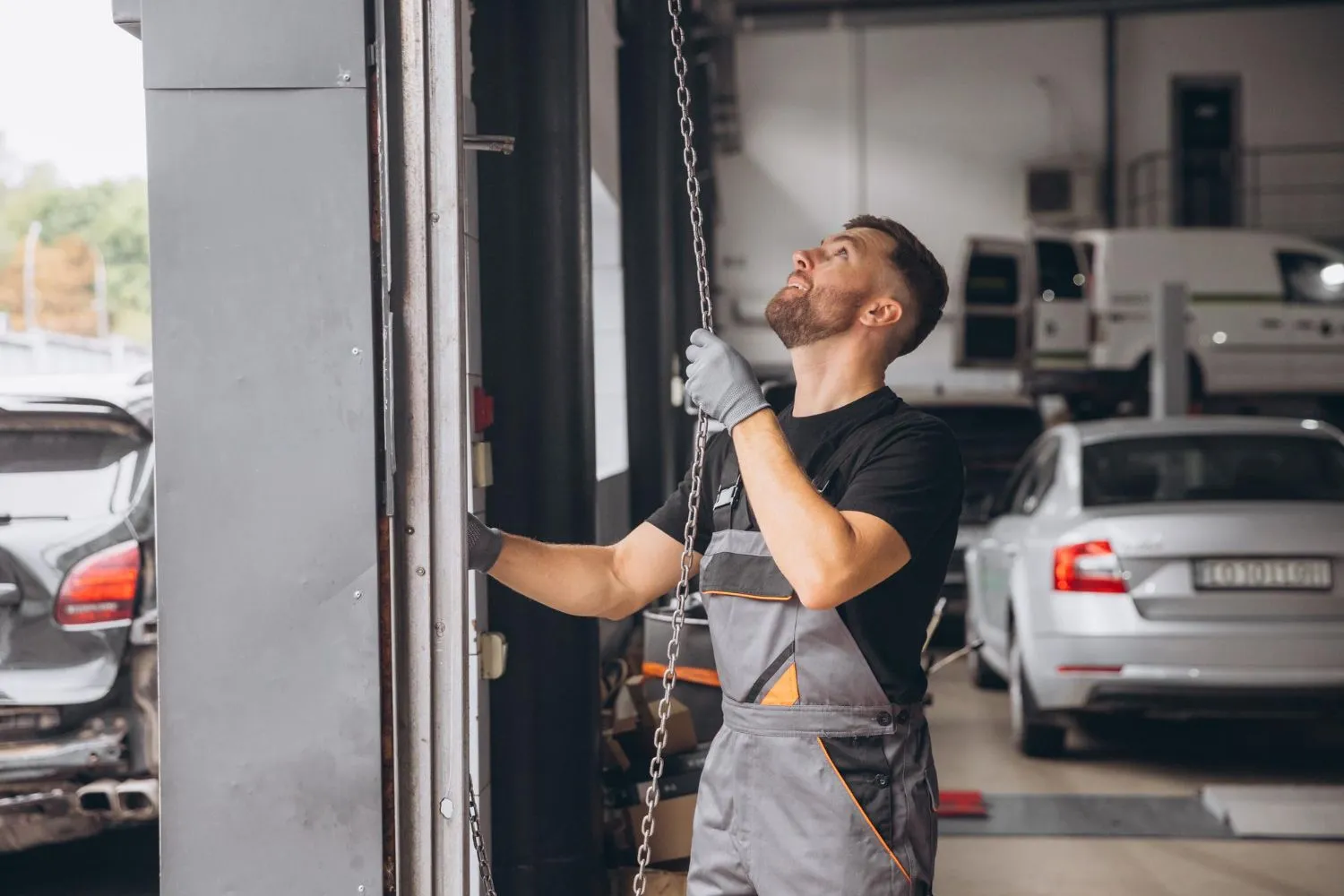 Technician pulling the manual chain hoist on a roll-up door at a vehicle workshop